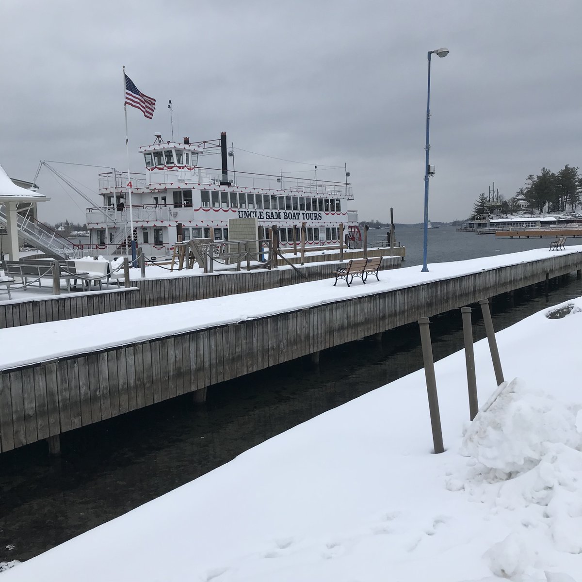 TIAssociation's tweet photo. Another gray and cloudy day in @MeetMeAtTheBay, but we are at least one day closer to next summer arriving! @BoatToursSam waiting patiently for next season with @BCResortMarina in the background! #1000islands #stlawrenceriver #thousandislands #summer2021 #alexbay https://t.co/P14zJfC57y