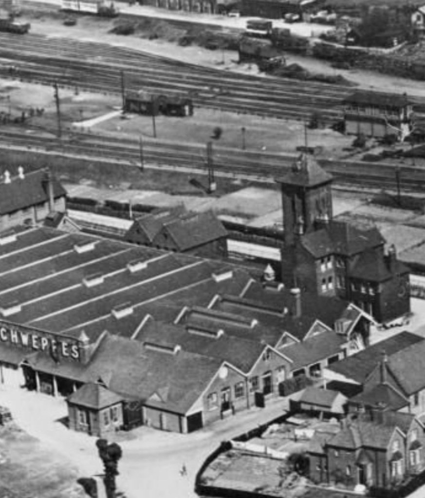 A 1921 Aerofilms photo of the Schweppes factory at West Hendon, and he railway and signal box behind it.Britain from Above image