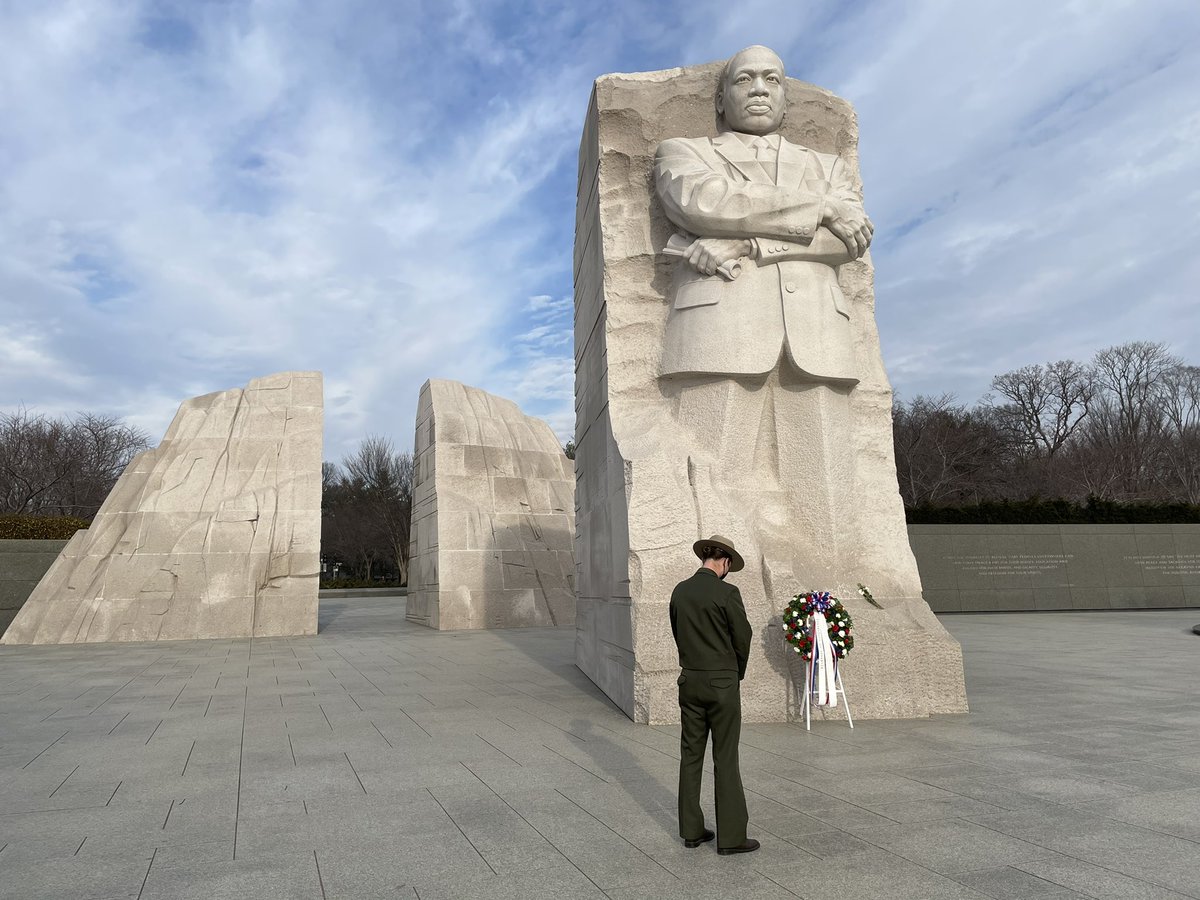 A uniformed park ranger standing by a wreath at the base of a large statue of Martin Luther King, Jr.