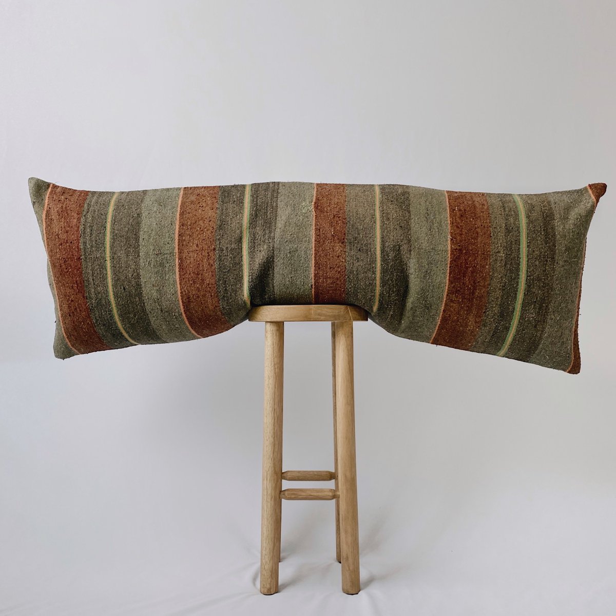 A pillow by Kaekoo Pillows set on a stool with a beige background.