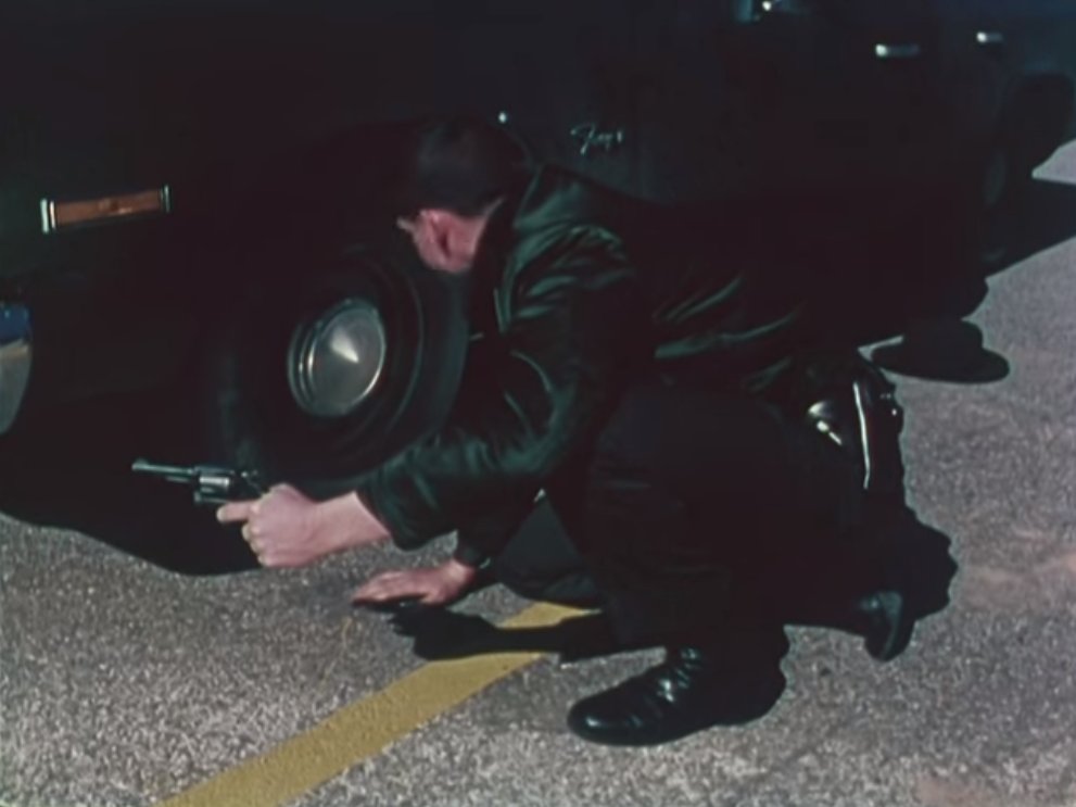 In another vignette an officer takes cover behind his vehicle. Revolver drawn he's positioned himself behind the off-side wheel of his car for protection against ricochets.