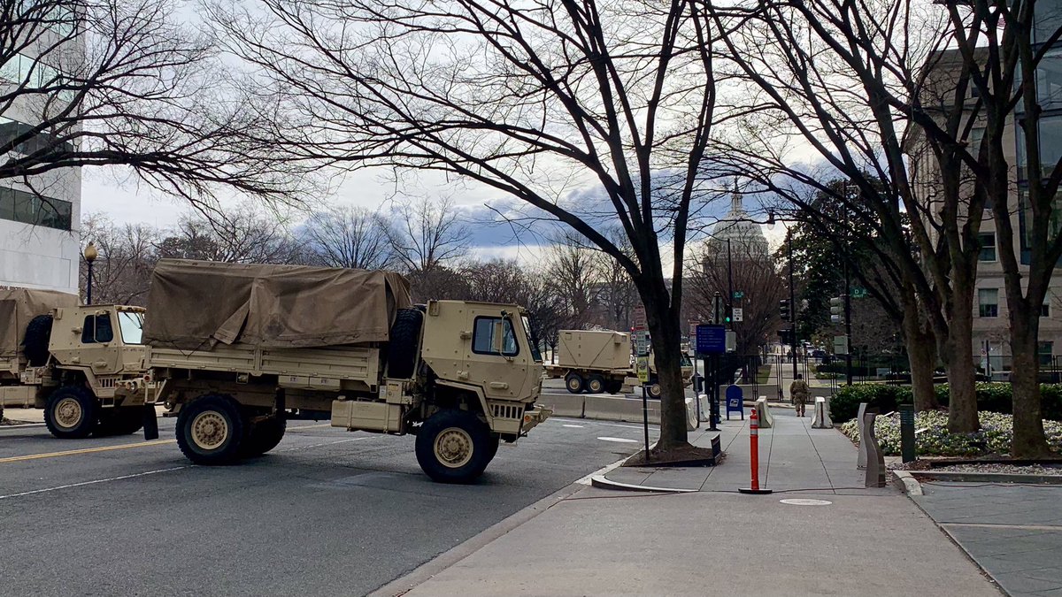 The Capitol seen through trees, behind a barricade of military vehicles 10/