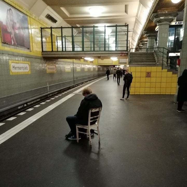 Ein Mann sitzt am Bahnsteig einsam auf einem Holzstuhl.