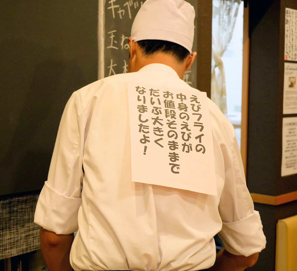 スペースの有効活用？とんかつ屋さんの店長。何故か背中に張り紙をしてお仕事中。