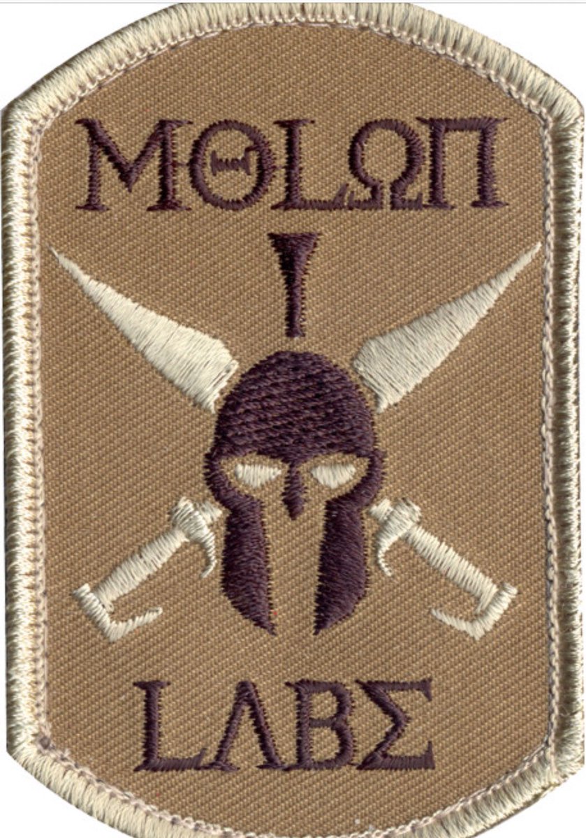 We have a match! Molon Labe patch on Magnolia’s arm has a Spartan helmet with swords crossing. Molon on top. Labe on bottom.Found at Army Universe. https://www.armyuniverse.com/brown-military-molon-labe-patch-with-hook-back.html