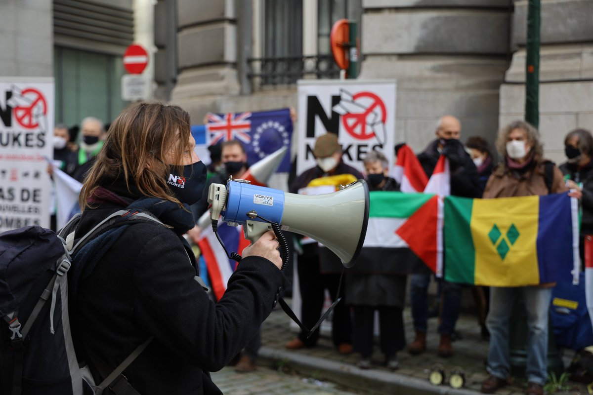 Brussels, belgium. At a street celebration masked woman holding a megaphone addresses a crowd with flags of the 50 states that have ratified the #nuclearban treaty and signs saying No Nukes. photo: Pax Christi Vlaanderen