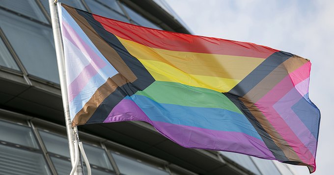 An image of the LGBTQ+ flag flying above City Hall 