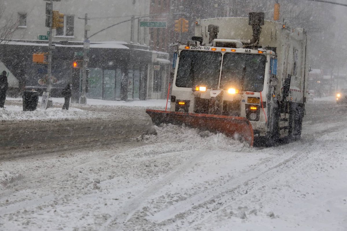 A white collection truck with a plow attached down the street.