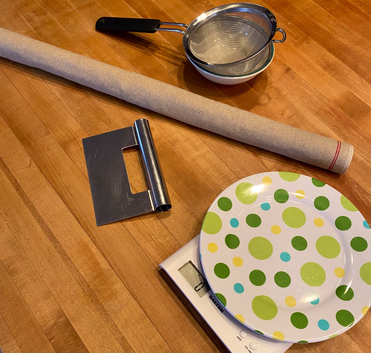 IT IS JUST ABOUT TIME to get started baking. This will take about three-and-a-half hours. Clear out a workspace. The coq avec chapeau Mardi Gras lamp is optional but preferred. You’ll also need the tools pictured: scale, pastry knife, sieve and bowl, and baguette couche.