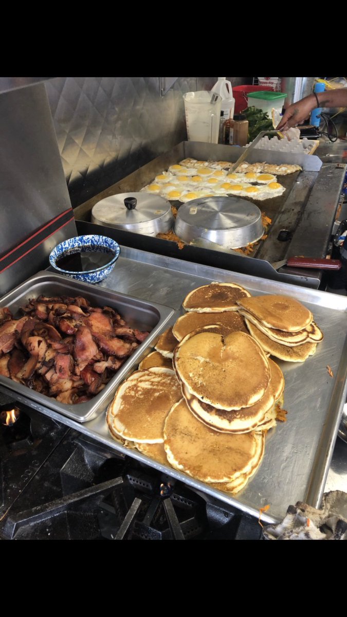 Lpts of fluffy pancakes, q bunch of eggs on the flat top and cooked crispy bacon on a pan