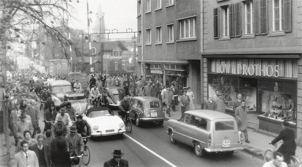 (9/10) Mittagsverkehr in Baden 1957. Die Autos sind immer noch in der Minderheit, beanspruchen aber gegenüber Fussgängerinnen und Radfahrern bereits den grössten Platz im Strassenraum.