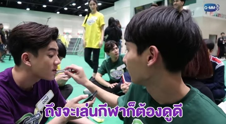 Gun applying lipbalm to Off's lips while the latter is playing on his phone 