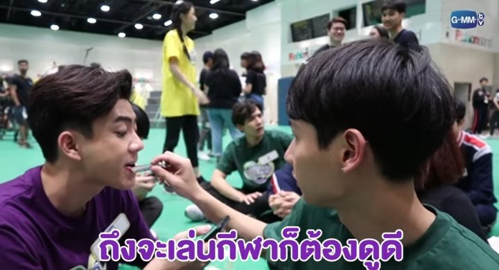 Gun applying lipbalm to Off's lips while the latter is playing on his phone 