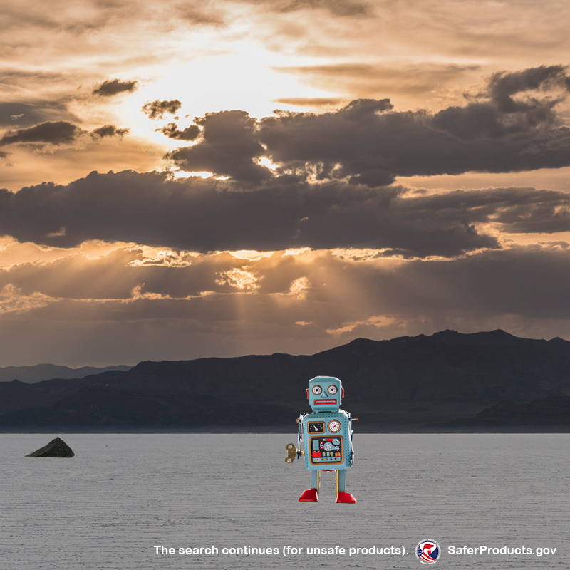 A robot walking alone in a desert while the sun rises in the background. The text reads: The search continues for unsafe products. SaferProducts.gov.