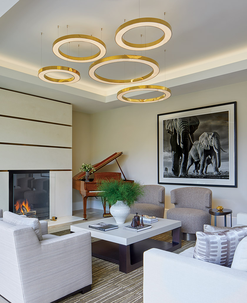 Satin-brass circular lights by <a href="/camerondesign/">Cameron Design House</a> bring drama to a family room; a custom fireplace surrounded by limestone &amp; brass provides warmth on chilly evenings.

Interior Design: M.S. Vicas Interiors
📸: Anice Hoachlander

Visit bit.ly/3aGE7Bm

 #top100designers