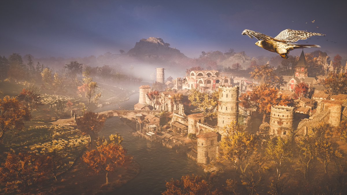 An eagle flies over the scene from the top left, facing the horizon, as rays of light fall onto the town below. The walled town is surrounded by brick towers and sits on the river's bank, an arched stone bridge leading from its entrance to the green field across the way, broken up by a patchwork of orange and brown leaved trees. A tall hill punctuates the skyline in the far distance.