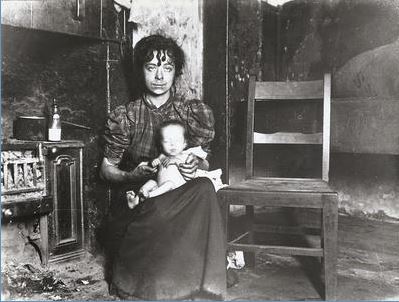 A woman and child pictured beside a kitchen range in slum property c 1910. The photograph may have been taken in connection with a scheme to provide poor mothers with milk for their babies. The following is the story of a practice that we take for granted today; the importance