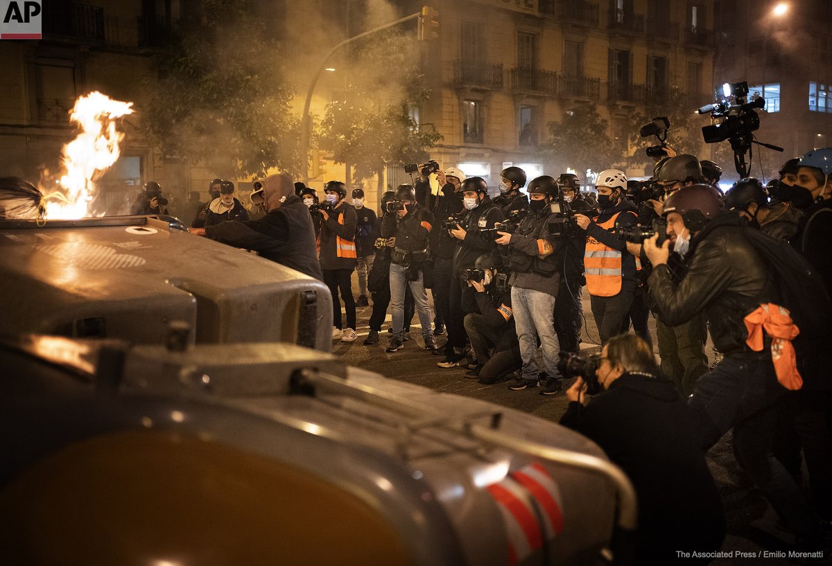 EmilioMorenatti's tweet photo. Media take images as demonstrators make barricades and burn trash containers during a protest condemning the arrest of rap singer Pablo Hasél in Barcelona, Spain, Friday, Feb. 19, 2021. https://t.co/YewXKjPaFw