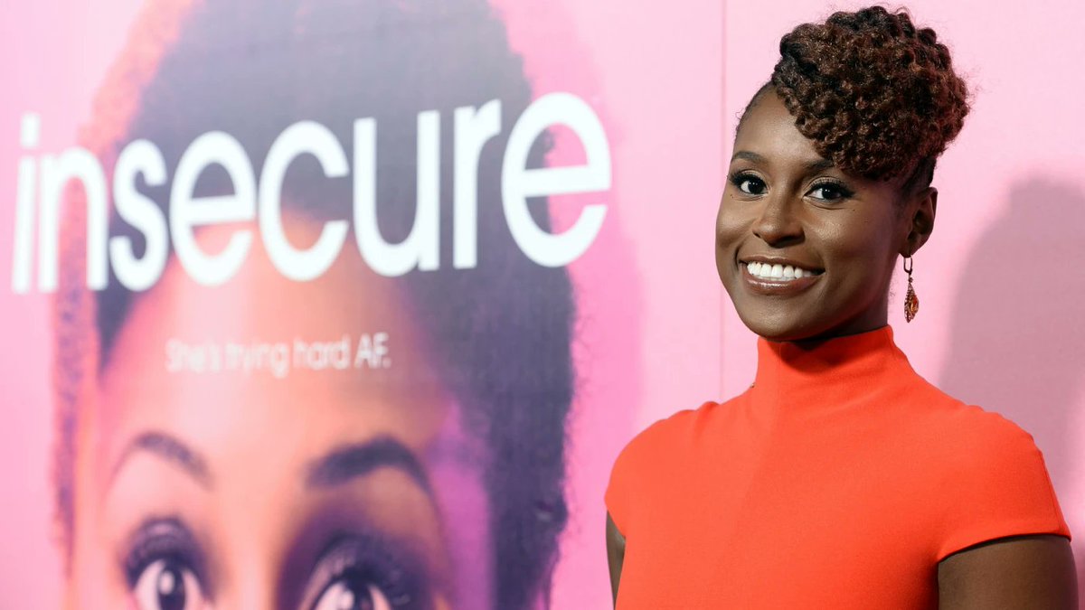 Issa Rae in front of an pink backdrop with her face and the name of her show, Insecure, wearing a red turtleneck