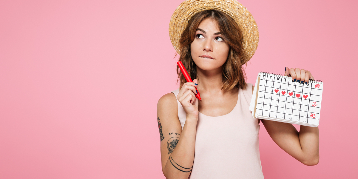 A tattooed woman with brown hair in a straw hat stands in front of a pink b...