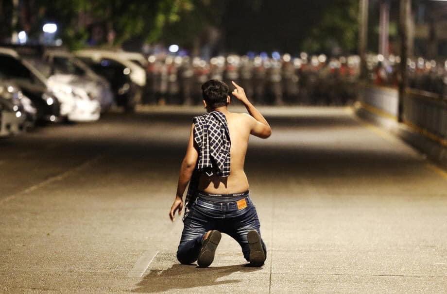 PyaePhyoViolin's tweet photo. A demonstrator kneels as he protests against the military coup while riot police advance on a street as tensions rise in Yangon, #Myanmar, 25 February 2021. #WhatsHappeningInMyanmar #MilkTeaAlliance https://t.co/ltHRg4VEaK