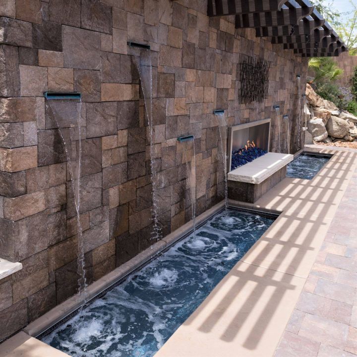 Need inspiration for your dream backyard? Check out this custom cascade wall with a central blue glass fire pit!