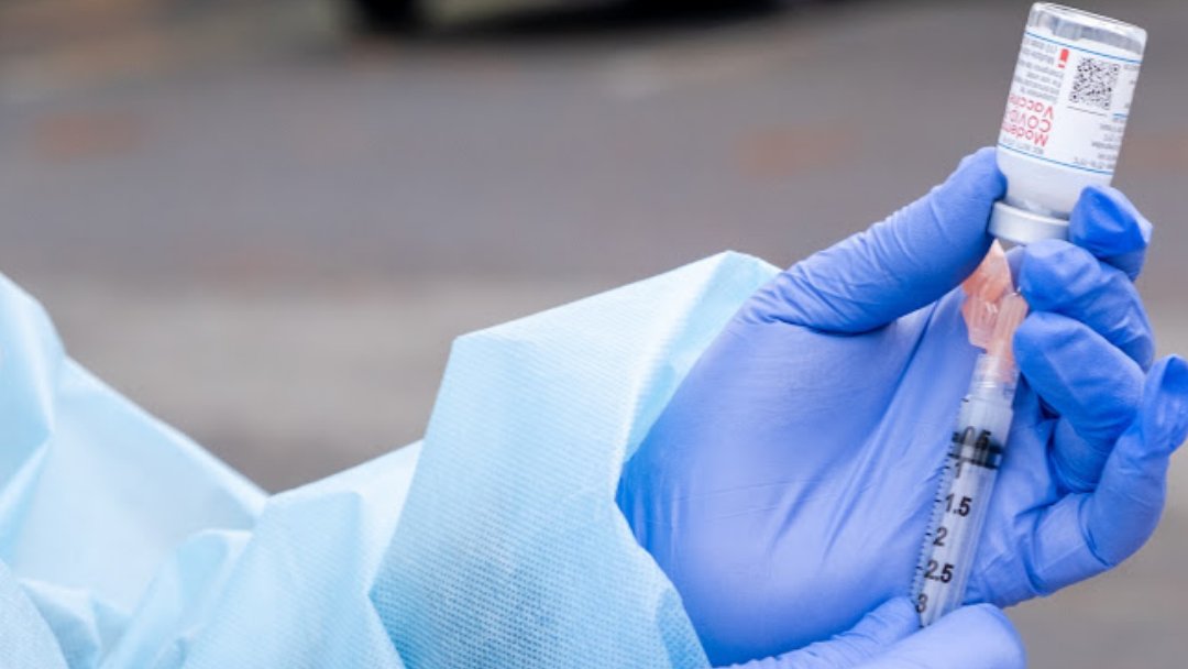 Photo depicting gloved hands taking COVID-19 vaccine out of a vial and into a needle for administering.