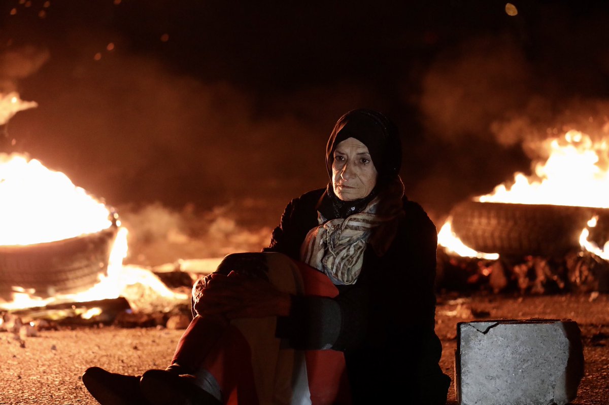 MatthieuKaram's tweet photo. An old lady sitting in front of burning tires during a demonstration in #Beirut tonight. The Lebanese pound has hit an all-time low today, trading at 10.000/$. #Lebanon sinking further more into a deep crisis. https://t.co/FiuLSGxmCv
