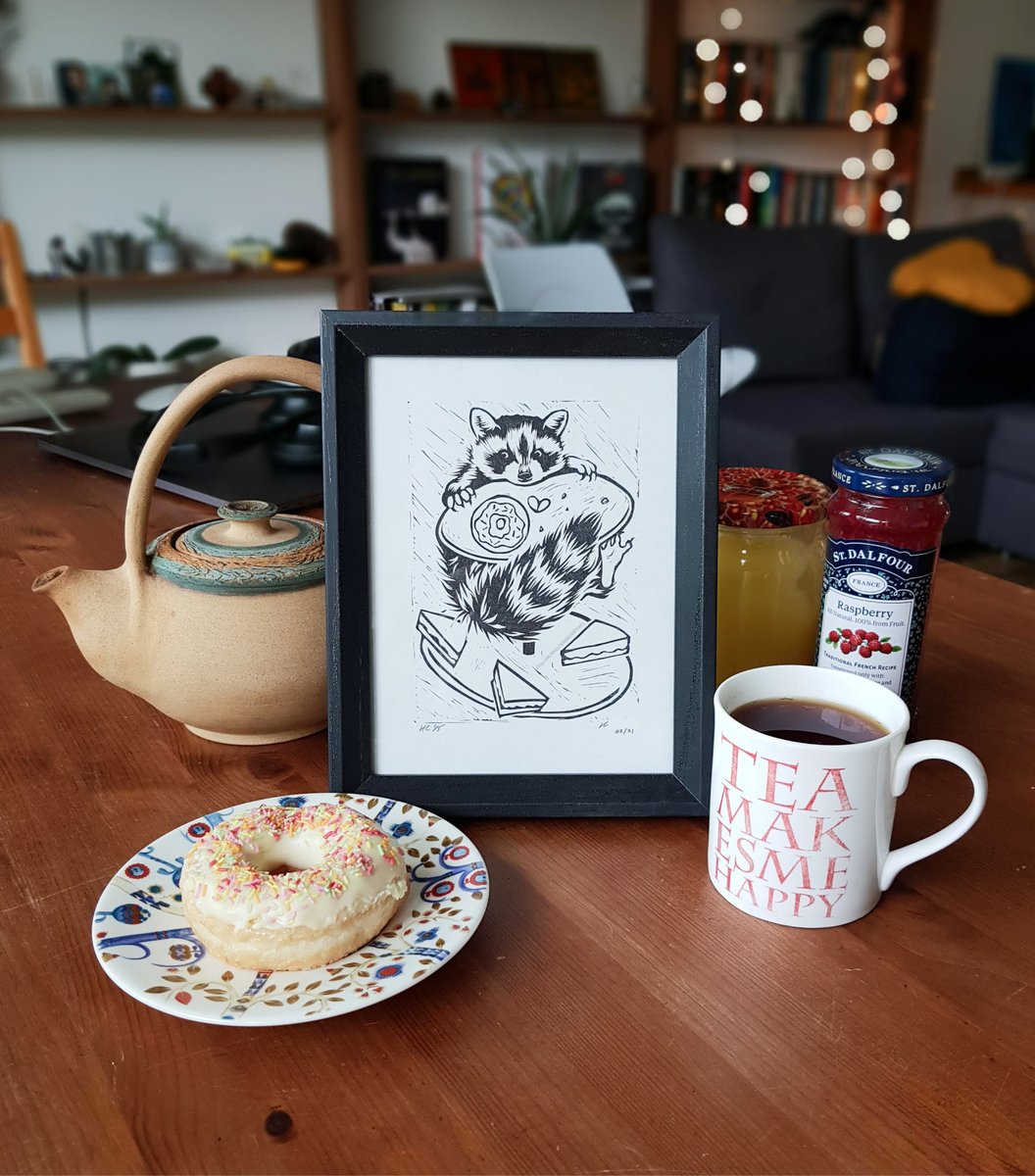 Black and white linocut print of a raccoon chasing a doughnut