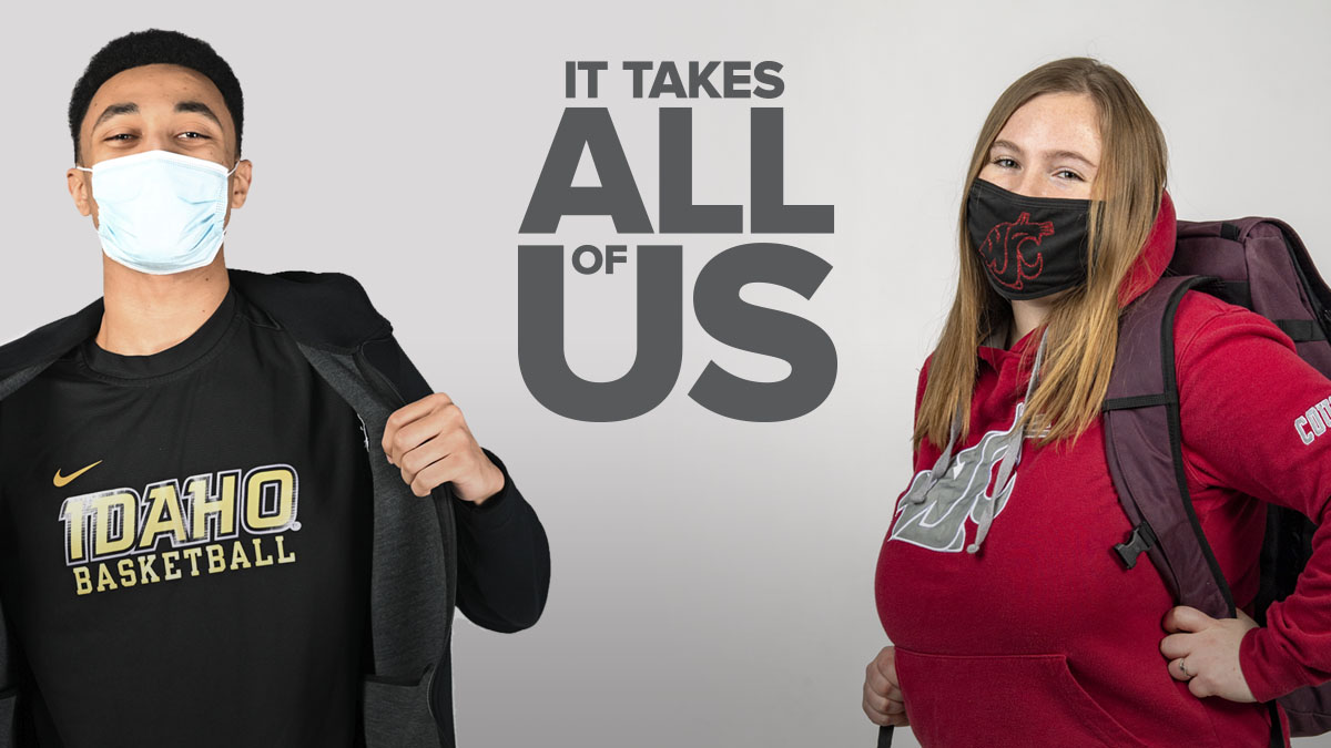 A University of Idaho student and a Washington State University student standing on either side of "It Takes All Of Us" script.