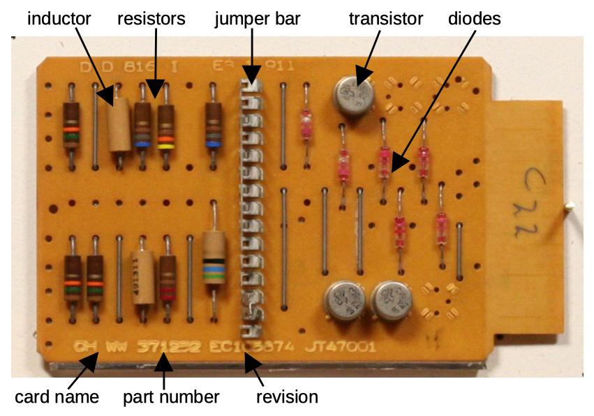 A circuit card, about the size of a playing card. It is a tan printed-circuit board with components mounted on it: inductors, resistors, transistors, diodes, and a jumper bar.