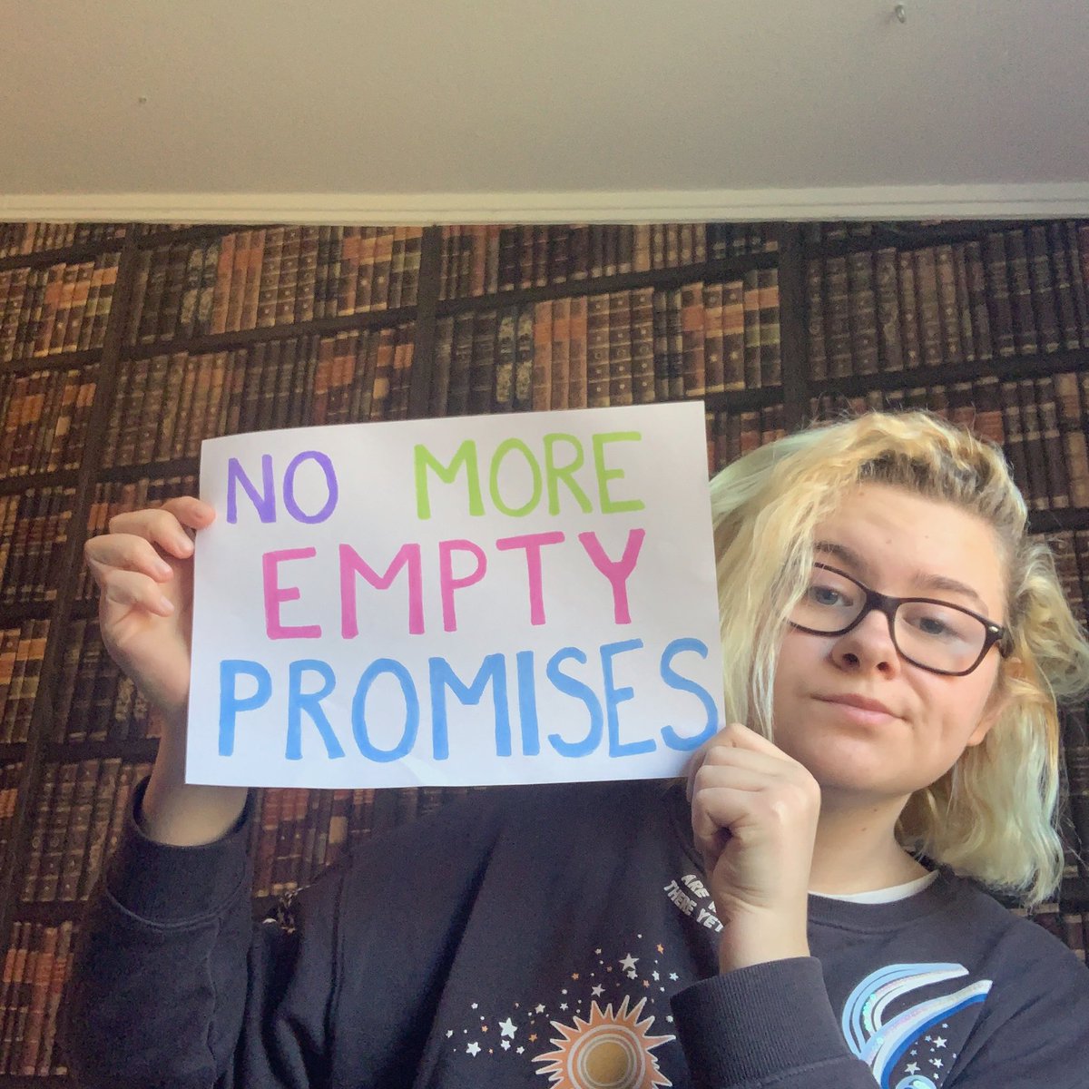 Selfie of a person holding up a sign that reads "No more empty promises".