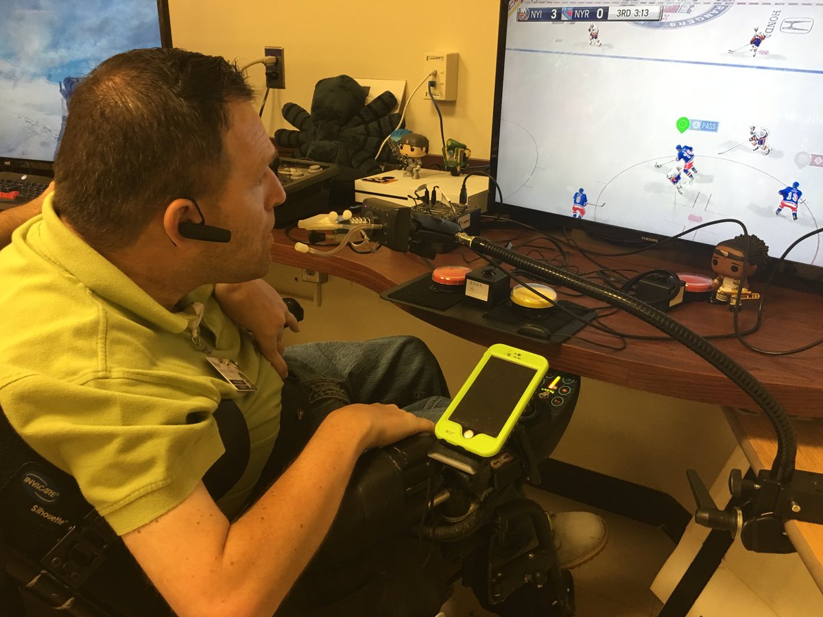 An intense looking adult male in a yellow T-shirt looks on from his yellow tinted wheelchair getting ready to play hockey for the first time