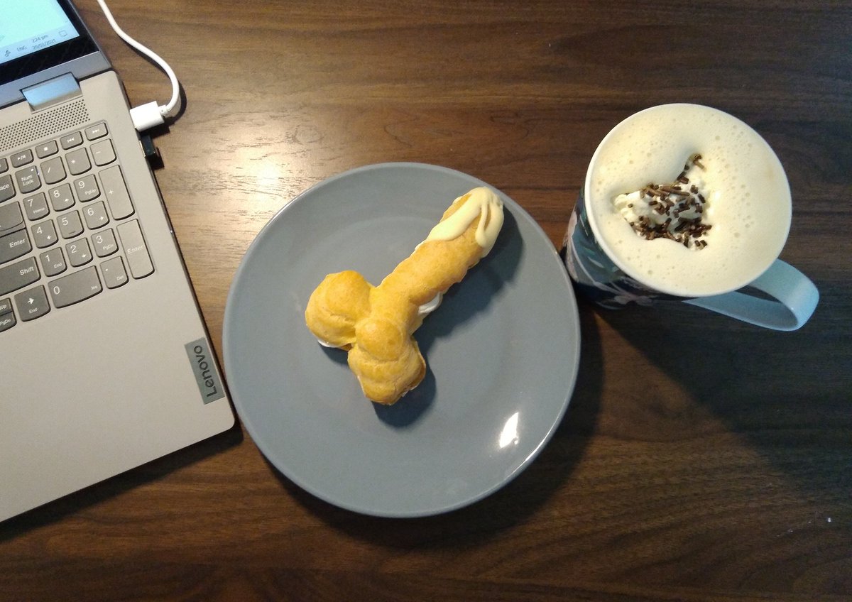 Photo is of a keyboard, a plate with a penis shaped eclair, and a cup of coffee with an accidentally heart shaped dollop of whipped cream on top.