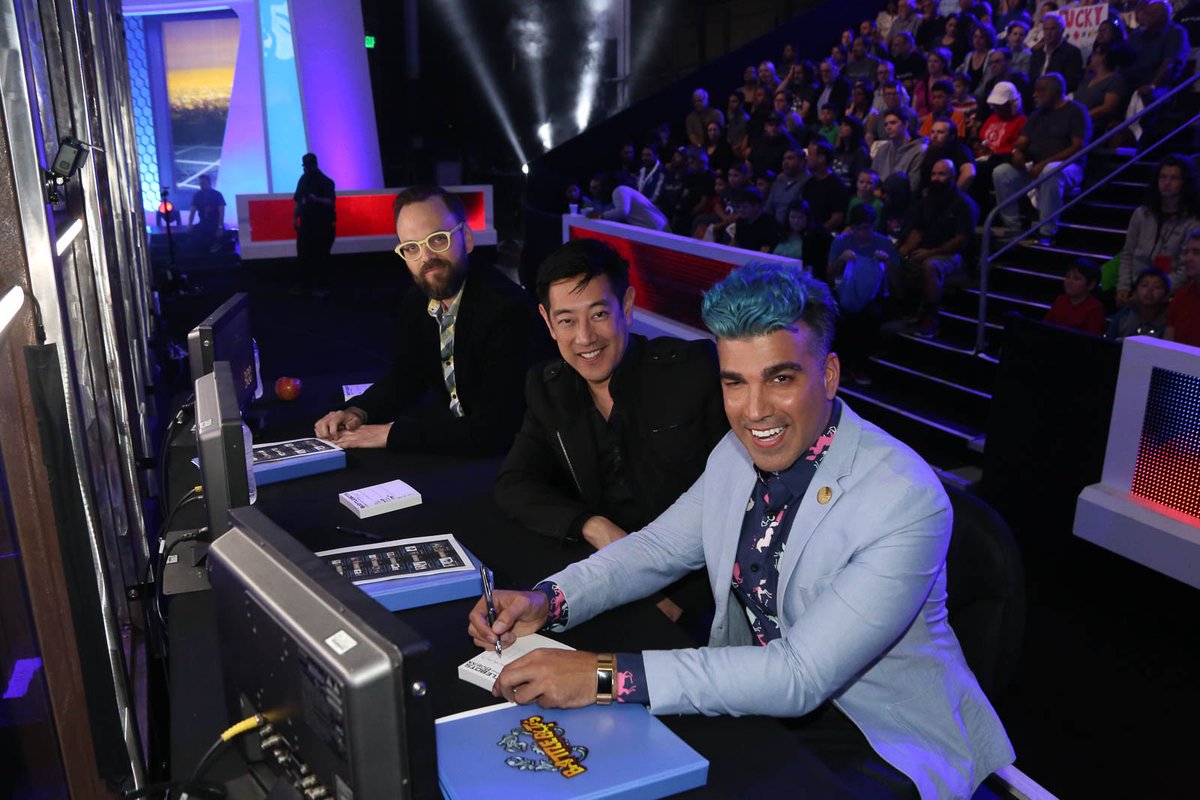 Three people sitting at judges table in BATTLEBOTS arena, Derek, Grant, Bobak