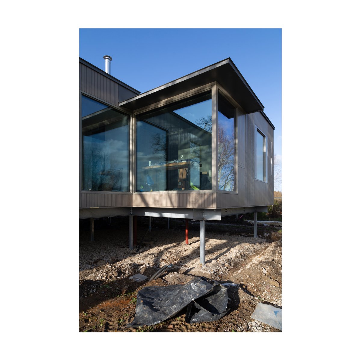 Glass corner window to fitness room floats over the garden at March House. The house is on stilts to raise it above the floodwaters of the River Thames.