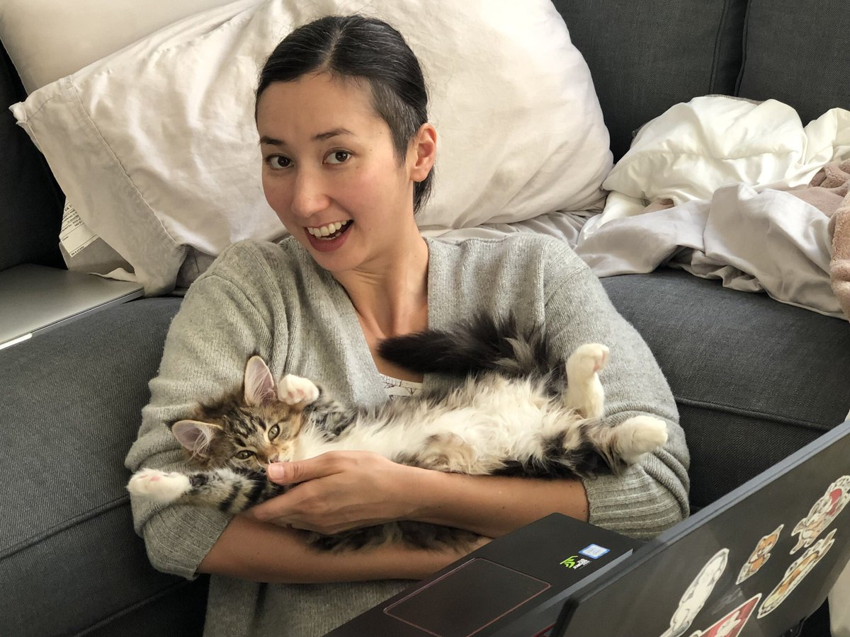 Me, holding a brown tabby Maine Coon kitten like a baby. All four paws are in the air as she looks at the camera. She juuuuust fits in my arms