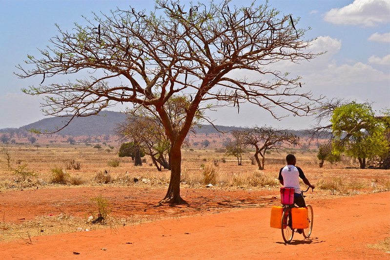 A person rides a bike with water jugs attached down a dirt road.