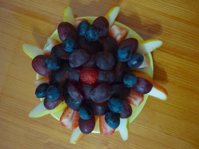 Geometric fruit arrangement on a plate. Used a pear and a pluot, each sliced in eight, three strawberries, one whole, two sliced in four, eight rose grapes sliced in two and twelve black grapes.