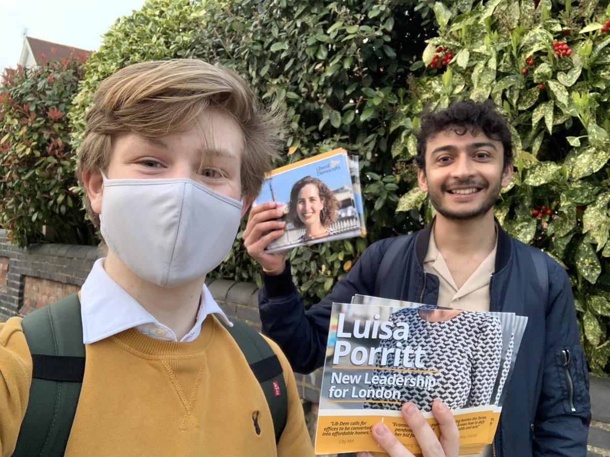 Two men holding ‘Luisa Porritt’ leaflets besides a bush.