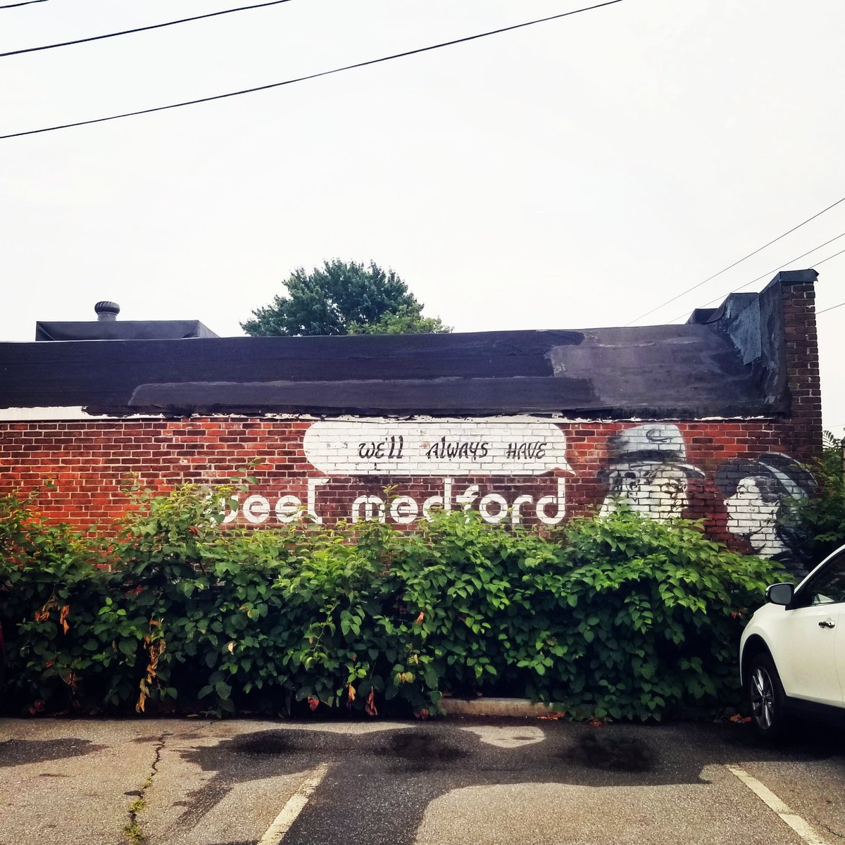 The side of a brick building has a black-and-white Casablanca-inspired mural that has a man and a woman and reads "We'll always have west medford."