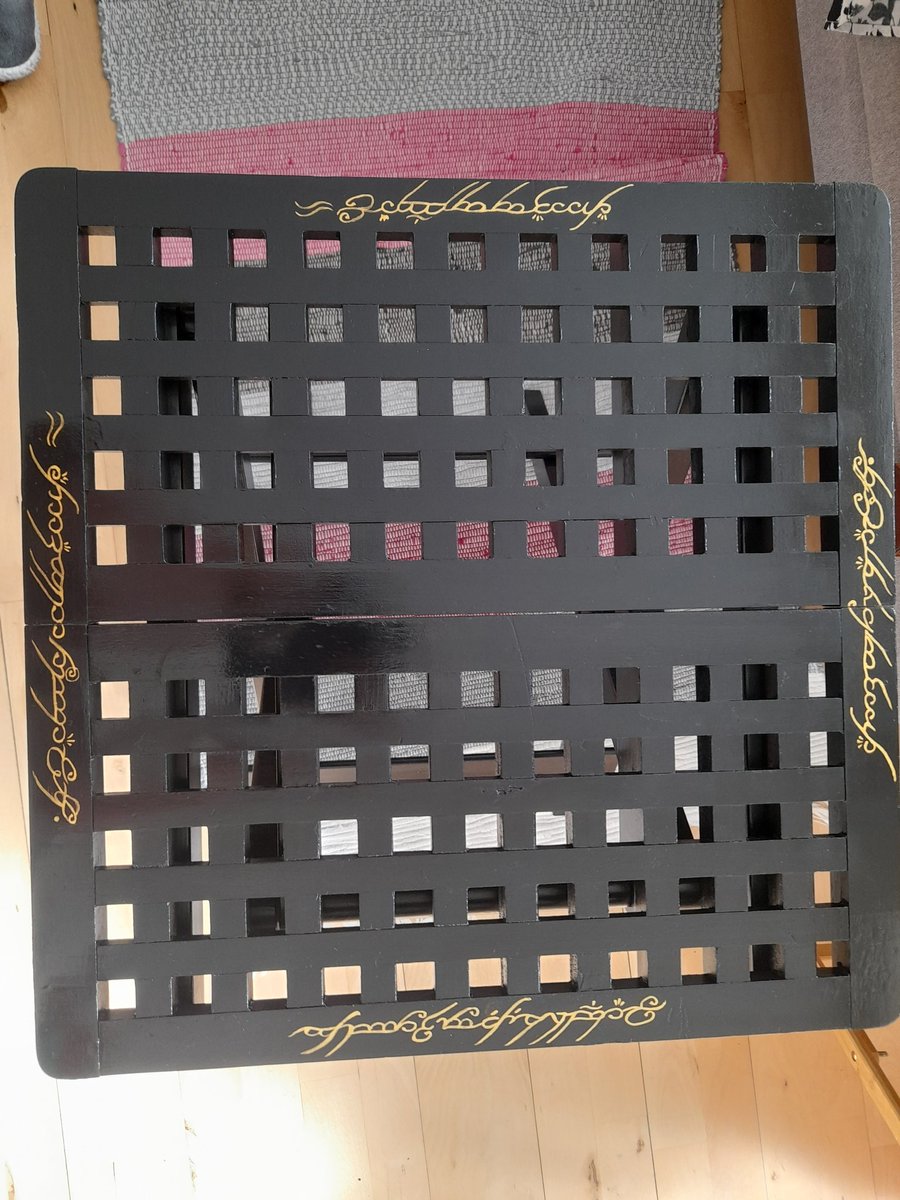 Apispaintbrain's tweet photo. BTW my mama bought me a little folding table to act as a coffee table. It was covered in barbecue sauce, candle wax and a mysterious white substance. I decided to freshen it up and needing it with the ring verse in black speech #nerdart #havingfunagain #flipit https://t.co/uYJFzIAcHW