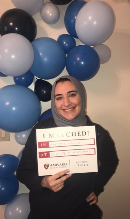 A student stands in front of balloons holding a sign that reads, "I matched!"