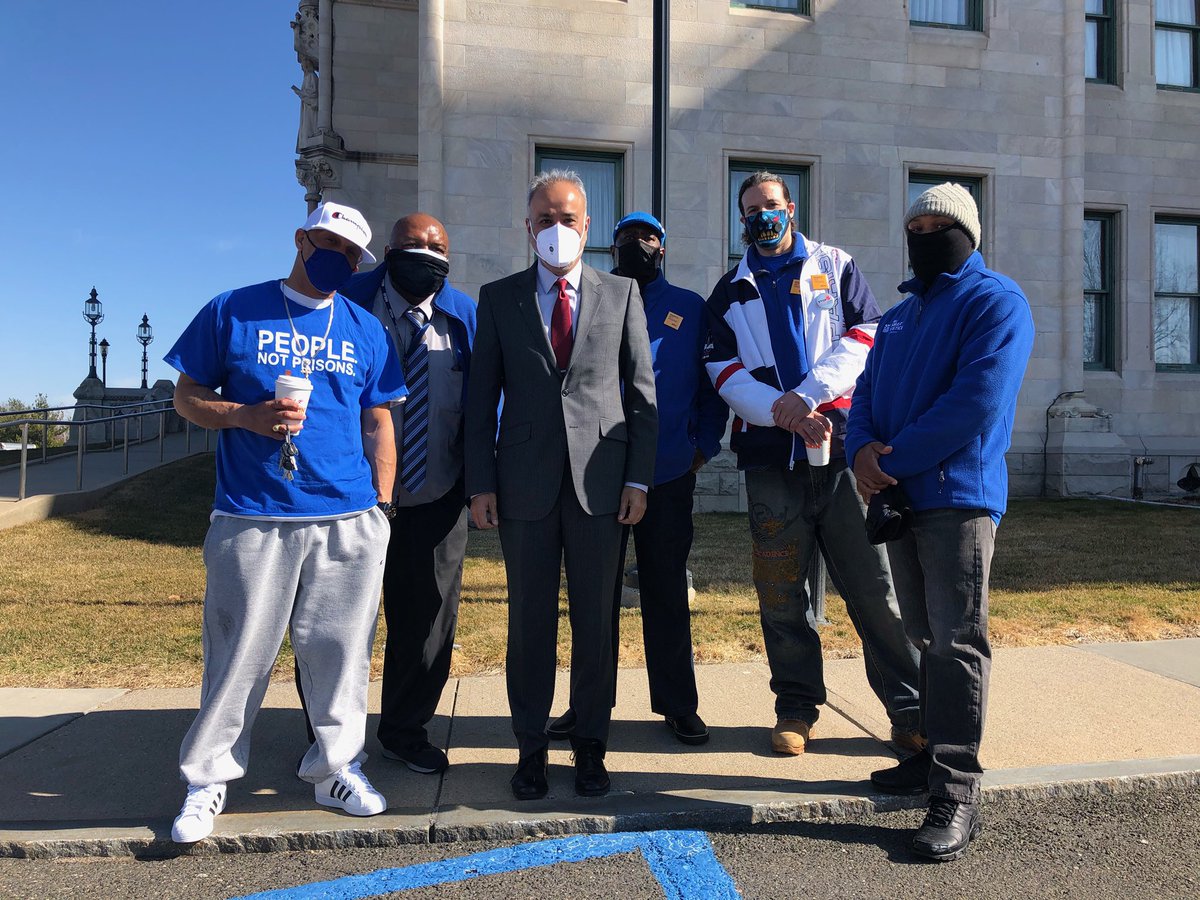 Five smart Justice leaders stand outside the CT capitol with Senator Saud Anwar. All are wearing masks and looking straight at the camera. Most leaders are wearing blue Smart Justice people not prisons shirts or zip up sweatshirts. The sun is shining.