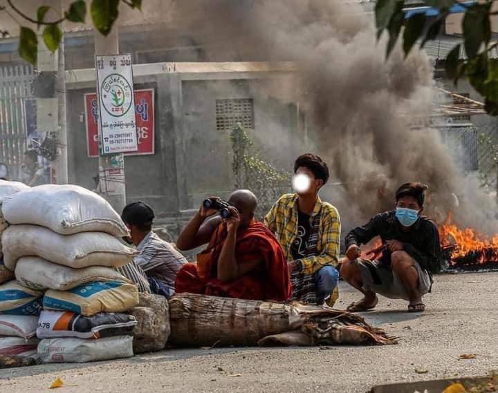 SuuMrat's tweet photo. A frontline scene of Spring Revolution in #Myanmar, where a monk is protecting young protestors by looking out for enemy military terrorists with binoculars. 
MOBILE DATA BLACKOUT
#WhatsHappeningInMyanmar  #Mar24Coup https://t.co/yfm2FX42oz