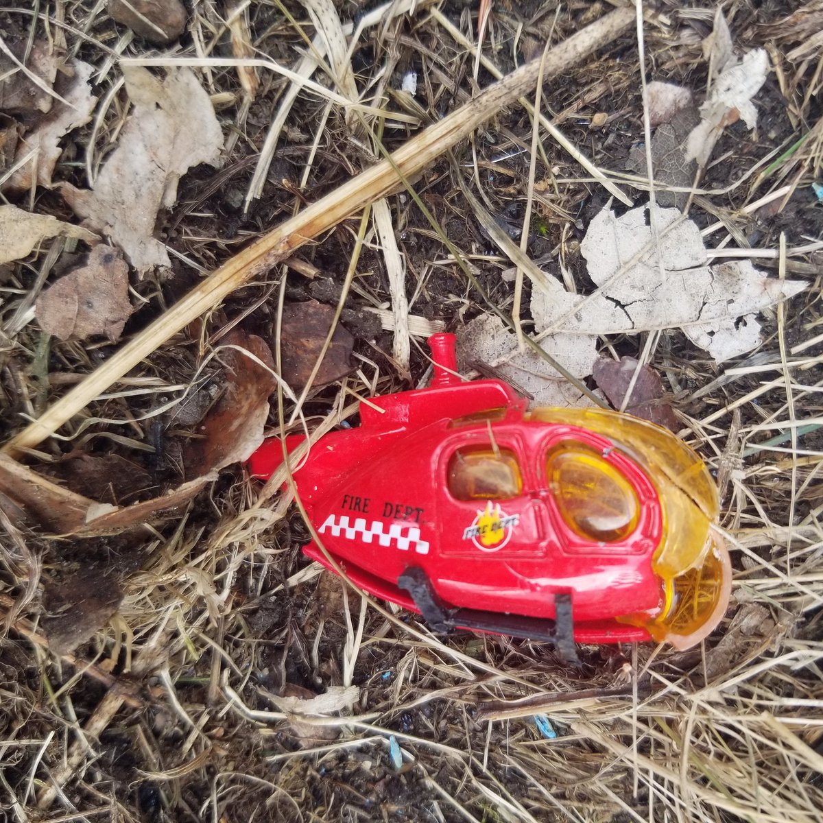 Broken red toy helicopter sits in dead grass