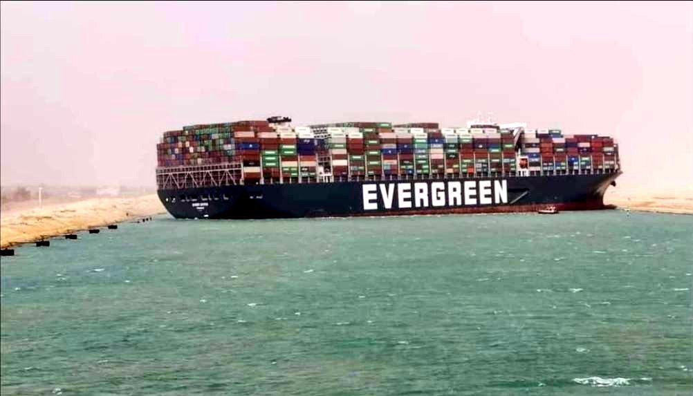 A large shipping vessel with the word "evergreen" on the side blocks a canal. 