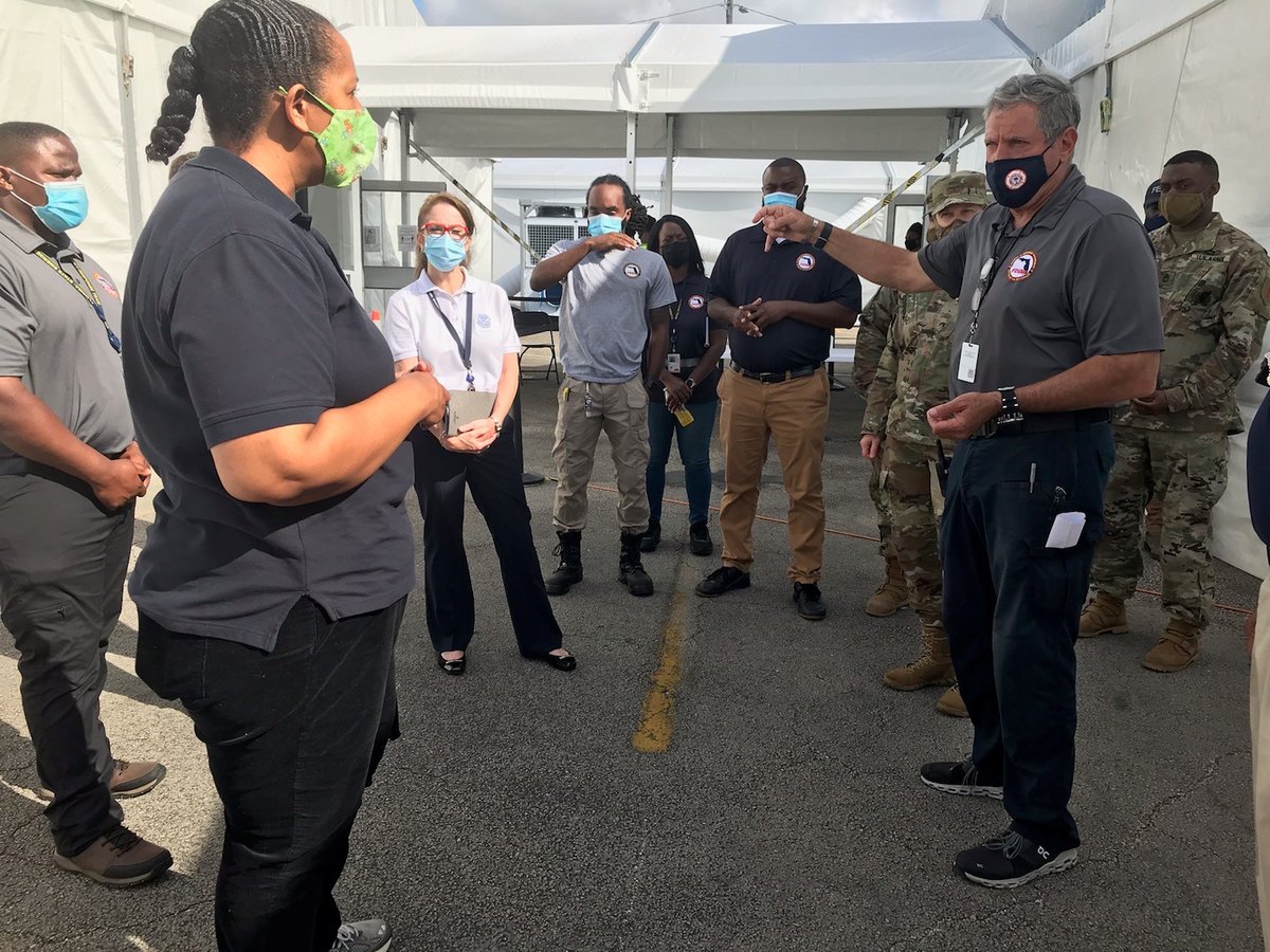 FEMA, FDEM and military personnel stand facing each other in circle. Man points as he speaks