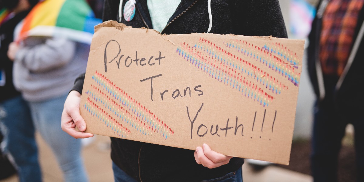 Close-up photo of a cardboard protest sign that reads "Protects trans youth!!!"