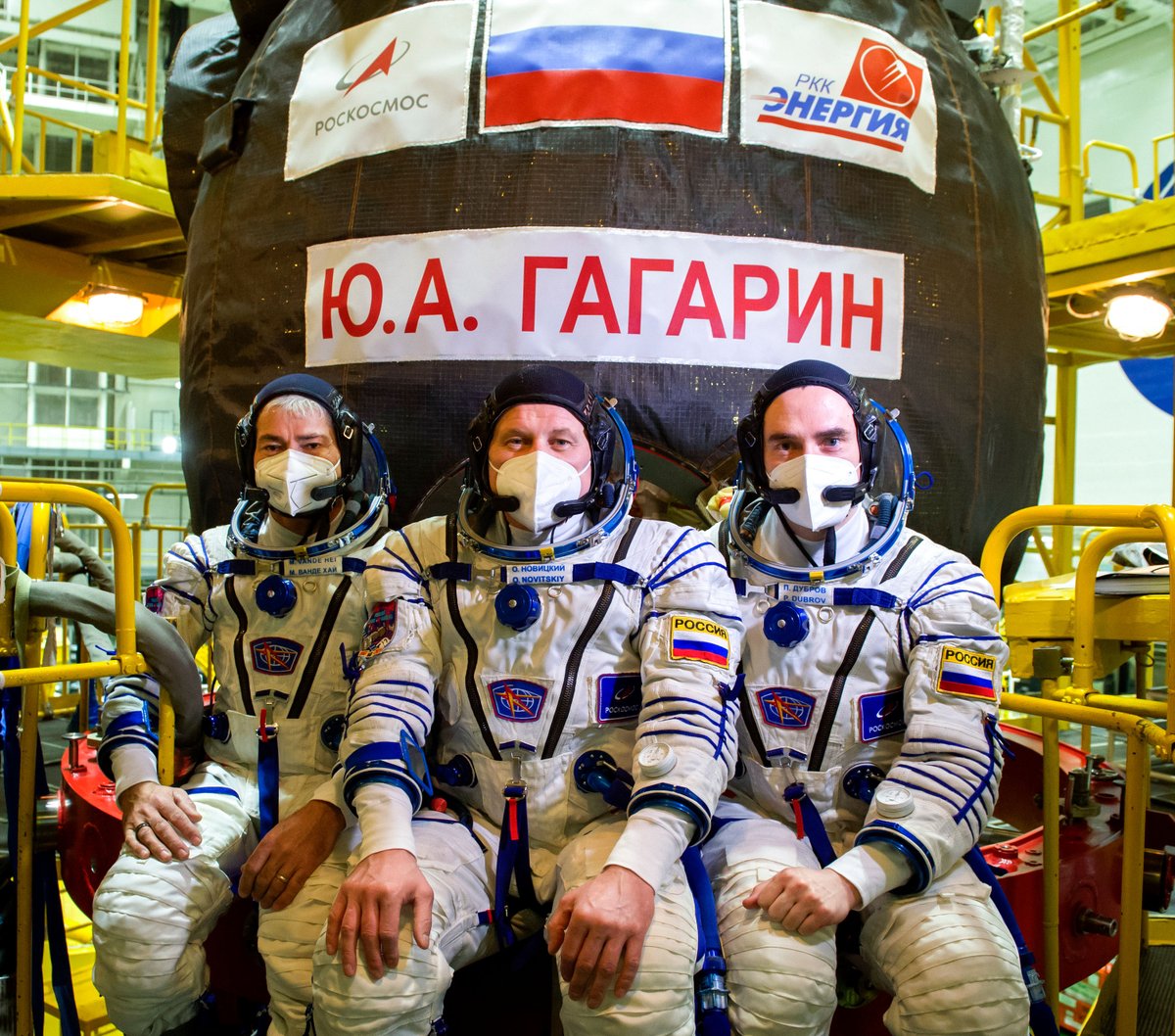 nhq202103270034 (March 27, 2021) --- Expedition 65 prime crew member NASA astronaut Mark Vande Hei, left, and Russian cosmonauts Oleg Novitskiy of Roscosmos center, and Pyotr Dubrov of Roscosmos, right, pose for a photo in front of the Soyuz MS-18 spacecraft, named after the first human to journey into space, Yuri Gagarin, after their fit check, Saturday, March 27, 2021 at the Baikonur Cosmodrome in Kazakhstan. They are scheduled to launch on a Soyuz rocket April 9. Photo Credit: (NASA/GCTC/Irina Spector)